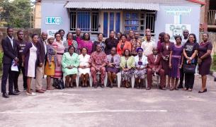 A large group of Nigerian adults poses formally for a photo where most are standing with a row of women seated in front