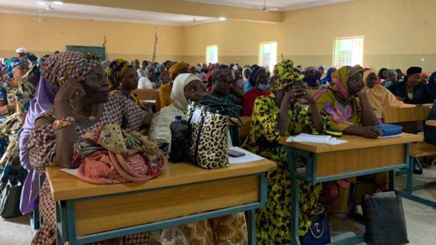 A room full of African women and men, many in colorful garments, sit at desks looking forward